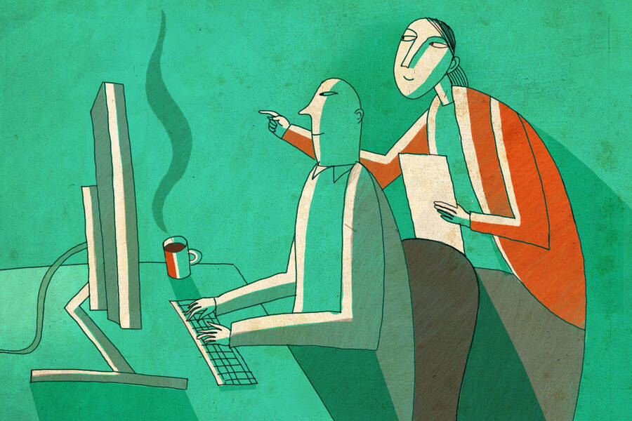 A worker helps another worker learn at a computer.